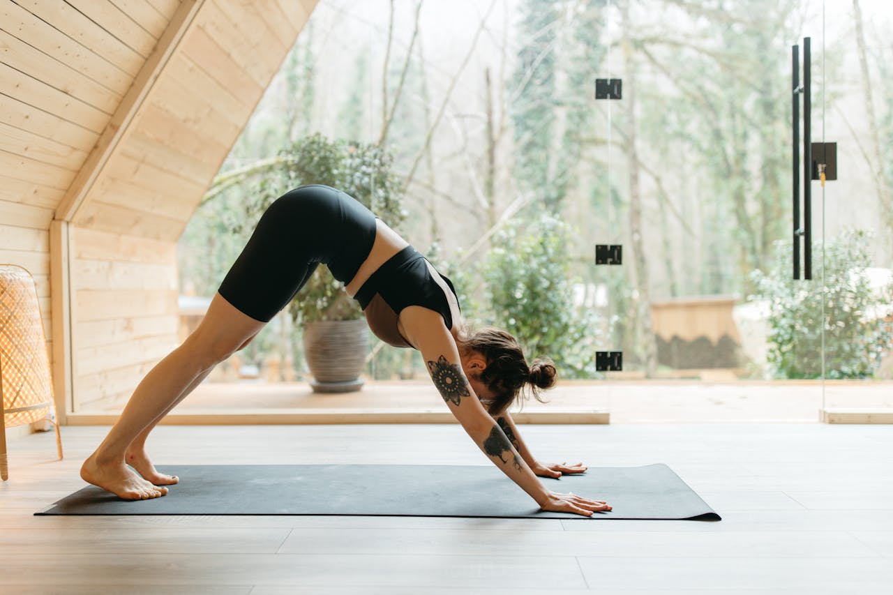 A woman performing the downward dog yoga pose on a mat in a serene indoor setting with natural light.