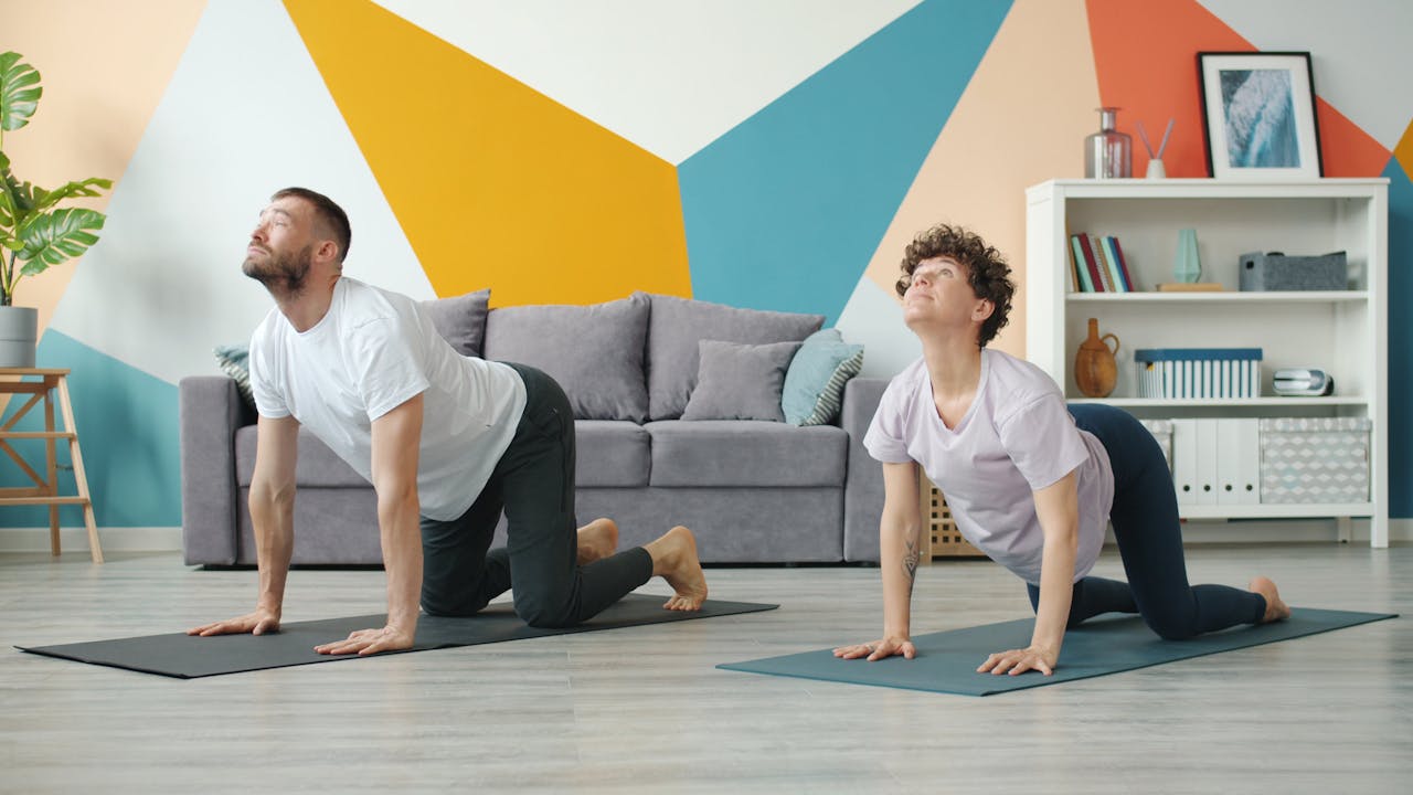 A couple doing yoga on mats in a modern and colorful living room setting.
