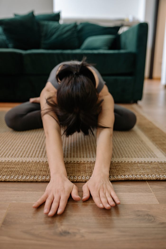 services-01 Woman performing yoga pose at home, stretching forward on a rug.